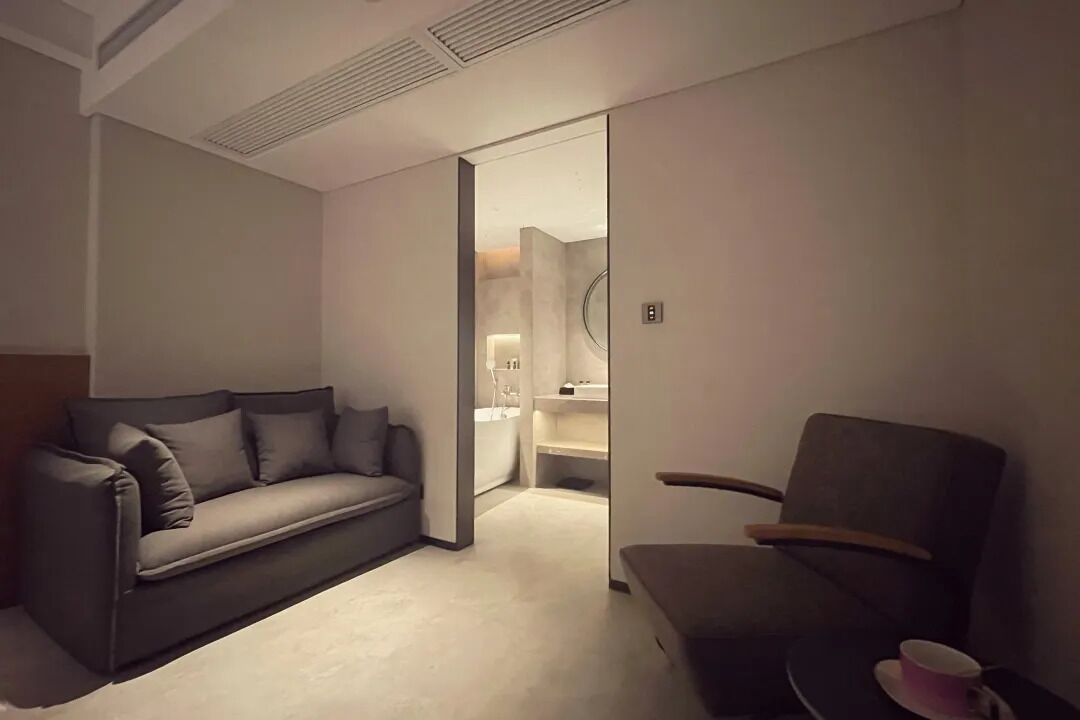 A modern hotel room with a sofa, a chair, and a small table with a cup.