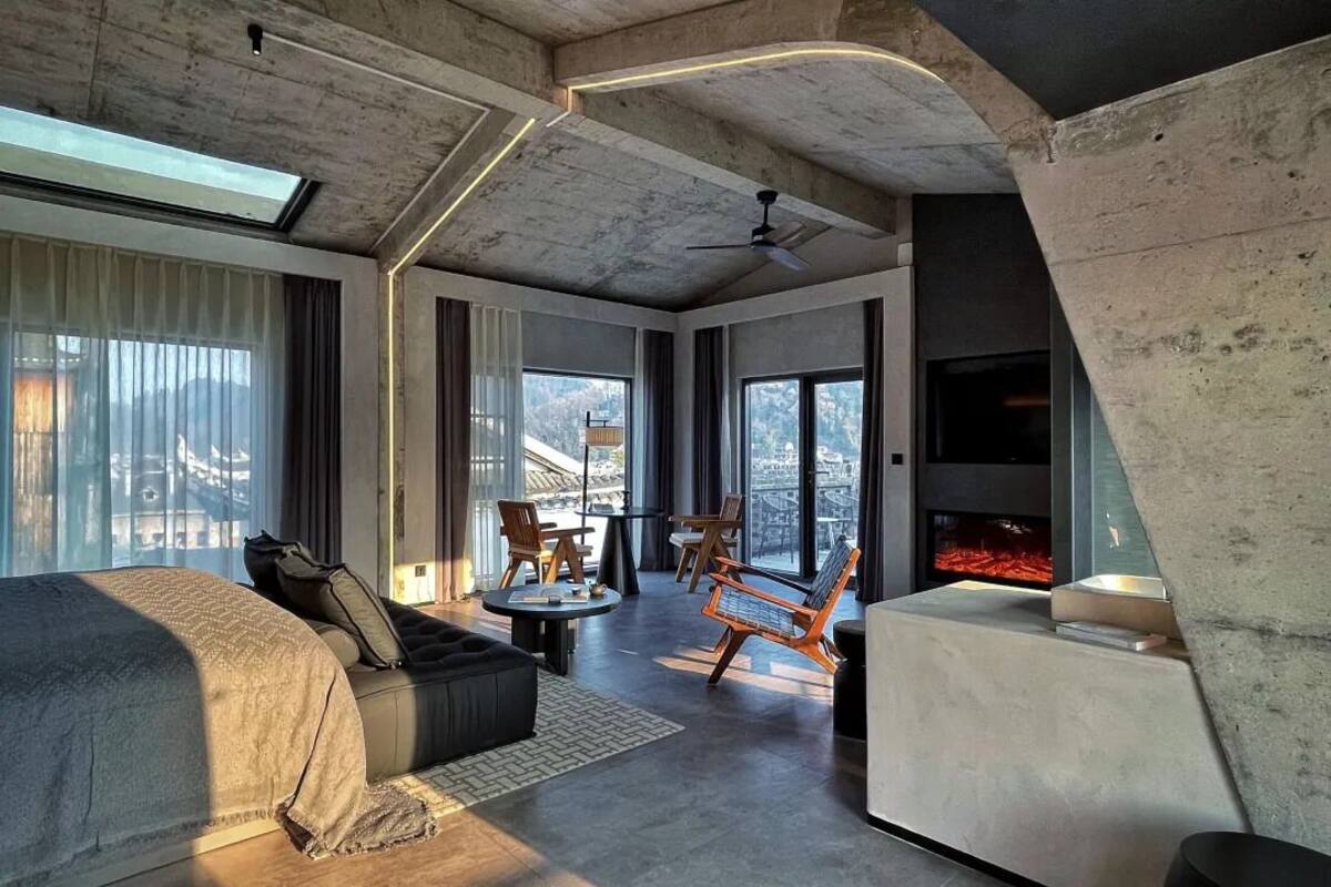 A modern hotel room with a large bed, seating area, and a fireplace.