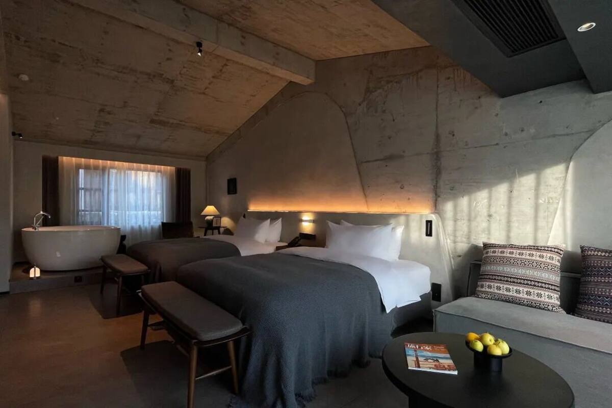 A modern hotel room with a large bed, a sitting area, a bathtub, and a small table with a magazine and lemons.