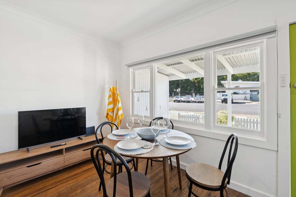 A dining area with a TV, dining table, chairs, and a view of a parking lot through large windows.