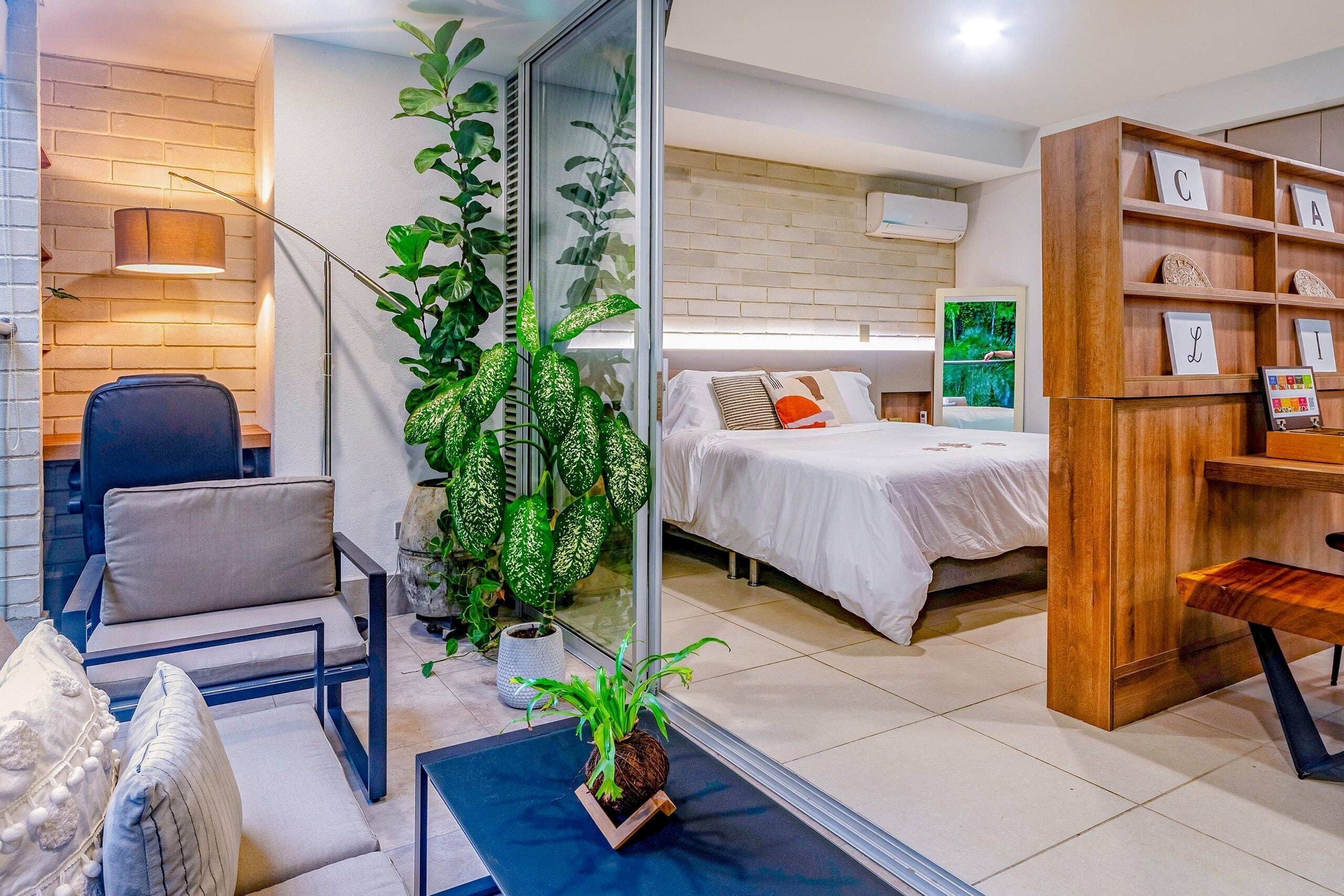 Habitación de hotel moderna con cama, escritorio, silla, estantería y planta en maceta.