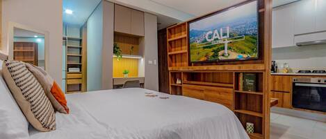 A bedroom with a bed, a TV mounted on a wooden shelf, and a kitchen area with a stove.