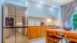 A modern kitchen with a stainless steel refrigerator, wooden cabinets, a coffee maker, and a dining area with a table and chairs. - Edificio Hayedo (Cali)