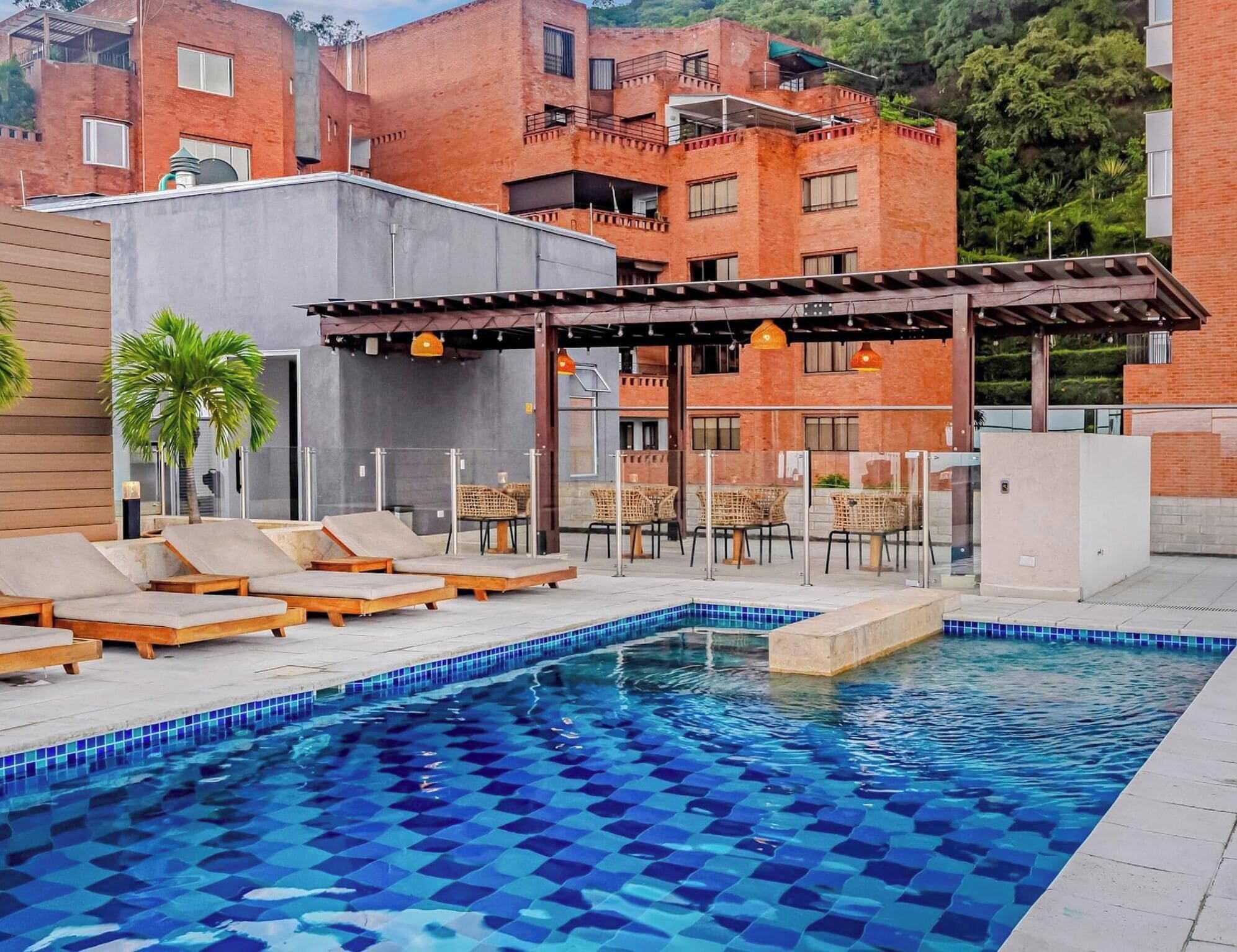 A swimming pool with a checkered tile pattern, surrounded by lounge chairs and a pergola with hanging lights.