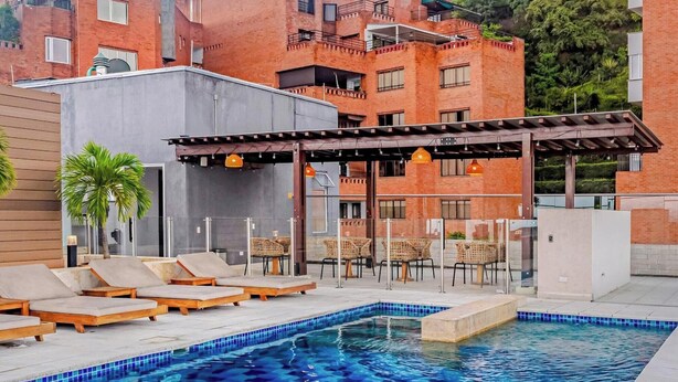 A swimming pool with a checkered tile pattern, surrounded by lounge chairs and a pergola with hanging lights. - Edificio Hayedo (Cali)