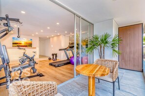 Ein modernes Heim-Fitnessstudio mit Trainingsgeräten, einem Holztisch und einem Korbstuhl.