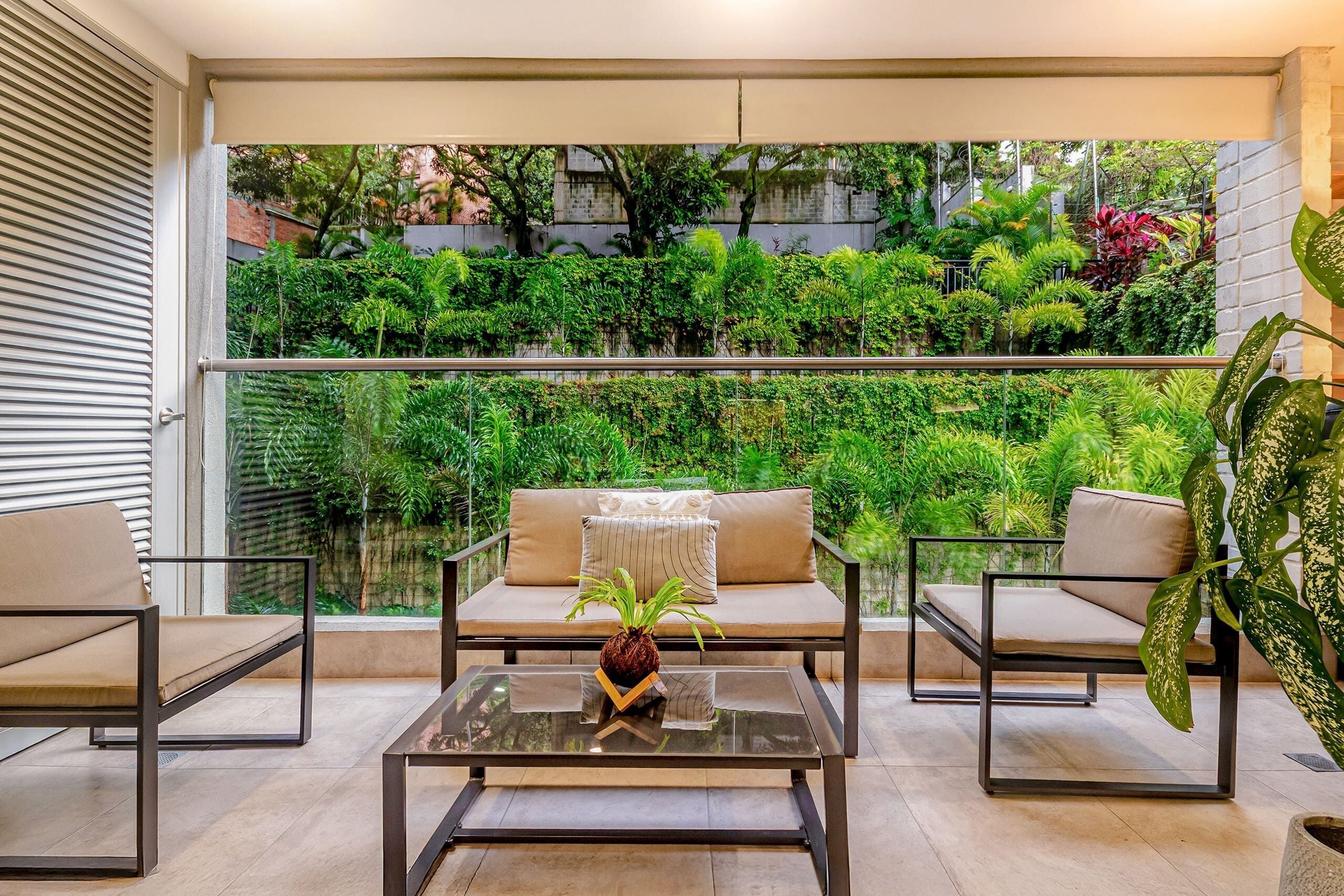A balcony with a sofa, two armchairs, a glass coffee table, and a potted plant.