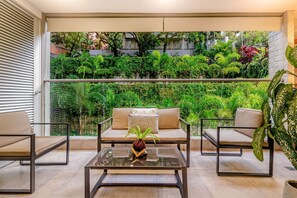 Ein Balkon mit einer Couch, zwei Sesseln, einem Glastisch und einem Topfpflanzen.