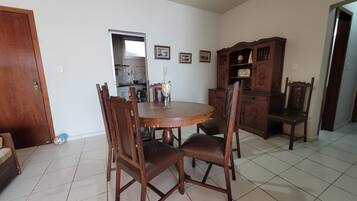 Uma sala de jantar com uma mesa de madeira redonda, quatro cadeiras, um armário e cozinha visível por uma porta aberta.