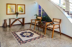 A room with a glass table, two wooden chairs, a patterned rug, and a vase with flowers.