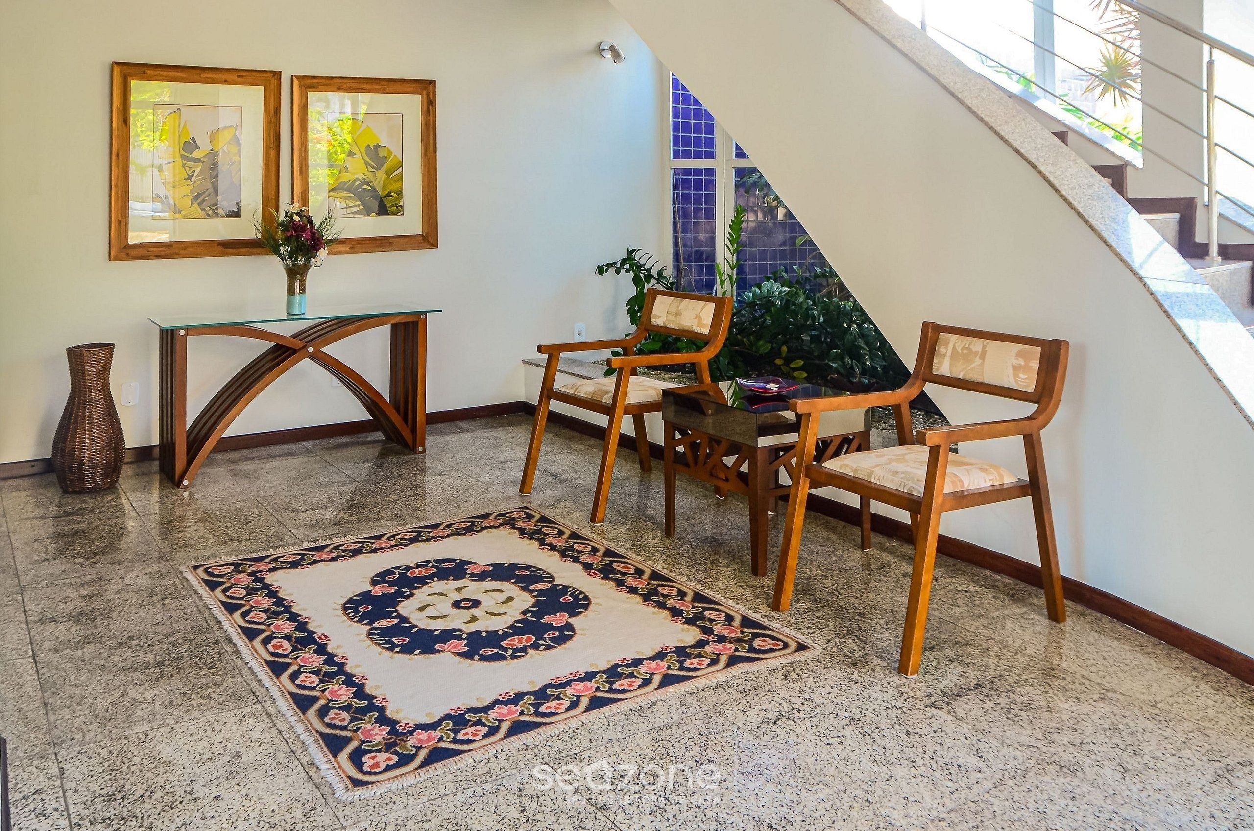 Ein Zimmer mit einem Glastisch, zwei Holzstühlen, einem gemusterten Teppich und einer Vase mit Blumen.