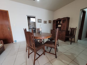 Un comedor con una mesa redonda de madera, cuatro sillas, un armario y una cocina visible a través de una puerta abierta.