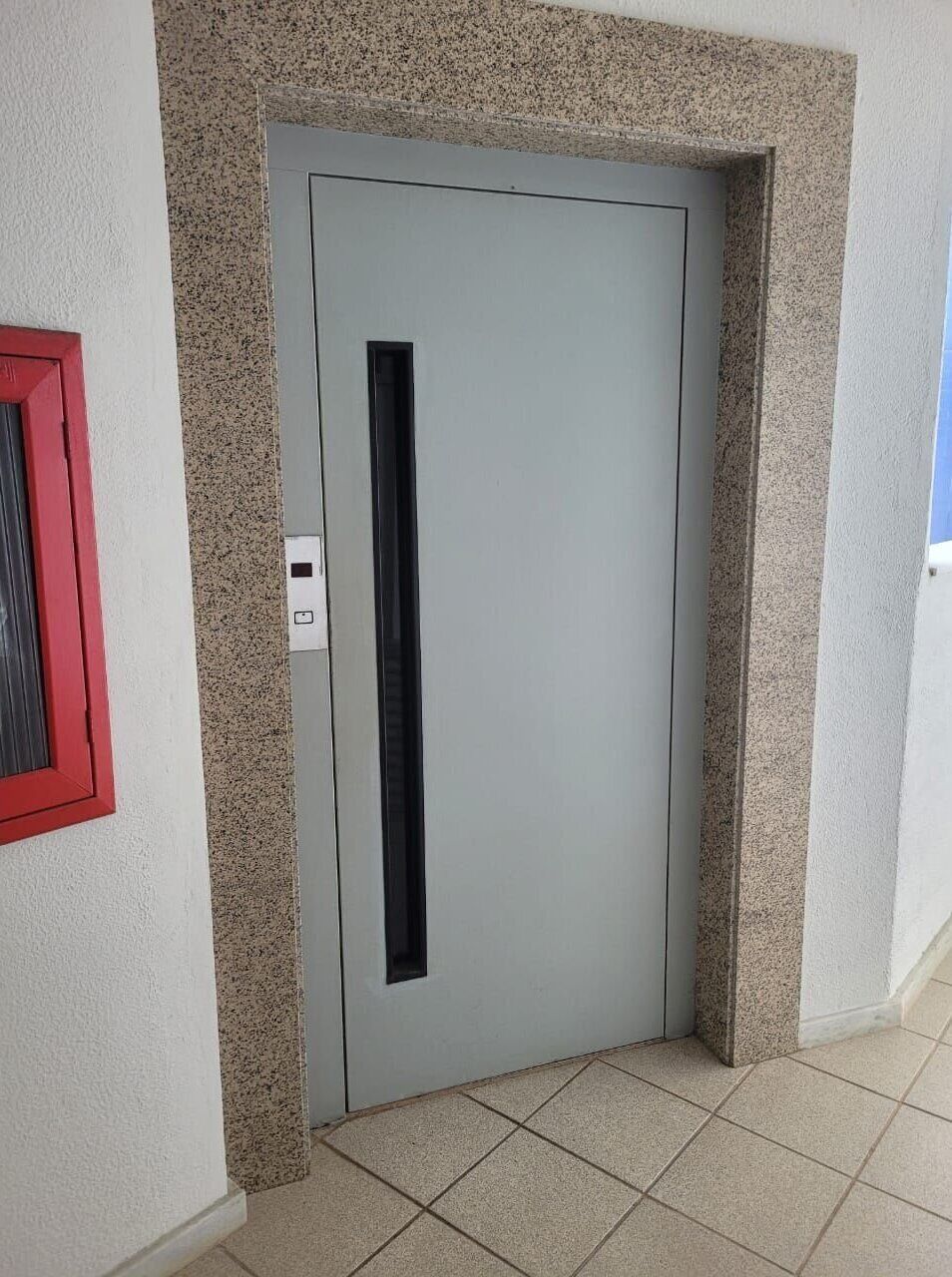 A door with a vertical handle, a red-framed window to the left, and a textured wall.