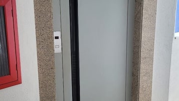 A door with a vertical handle, a red-framed window to the left, and a textured wall.