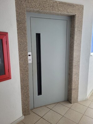 A door with a vertical handle, a red-framed window to the left, and a textured wall.