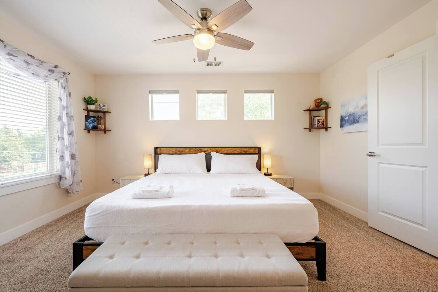 Une chambre bien rangée, avec un lit, des tables de chevet, un ventilateur de plafond et une porte.