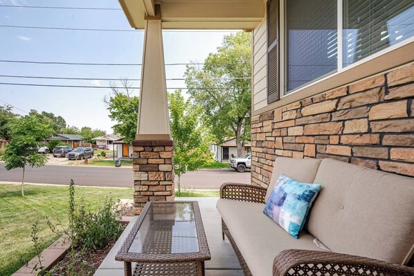 A covered patio with a glass table, wicker furniture, and a stone pillar.