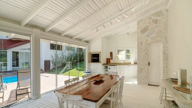 Un vaste espace d édié à la salle à manger, avec une table en bois et des chaises blanches, un mur en pierre et une vue sur une piscine.