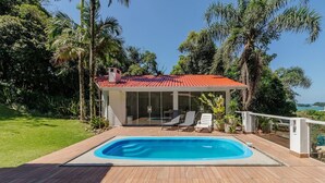 Un espace aménagé au bord de la piscine, comprenant une piscine rectangulaire, un coin salon couvert avec des chaises, et une vue sur la mer.
