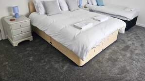A bedroom with a large bed, two bedside tables, and a smaller bed in the background.