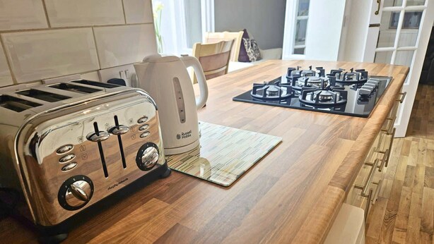 A kitchen with a wooden countertop, a toaster, a kettle, and a gas stove.