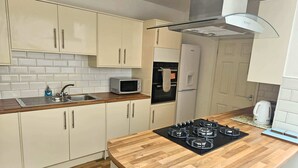 A modern kitchen with white cabinets, a wooden countertop, a gas stove, a microwave, and a kettle.