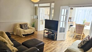 A living room with a leather sofa, a beige armchair, a flat-screen TV, and a wooden floor.
