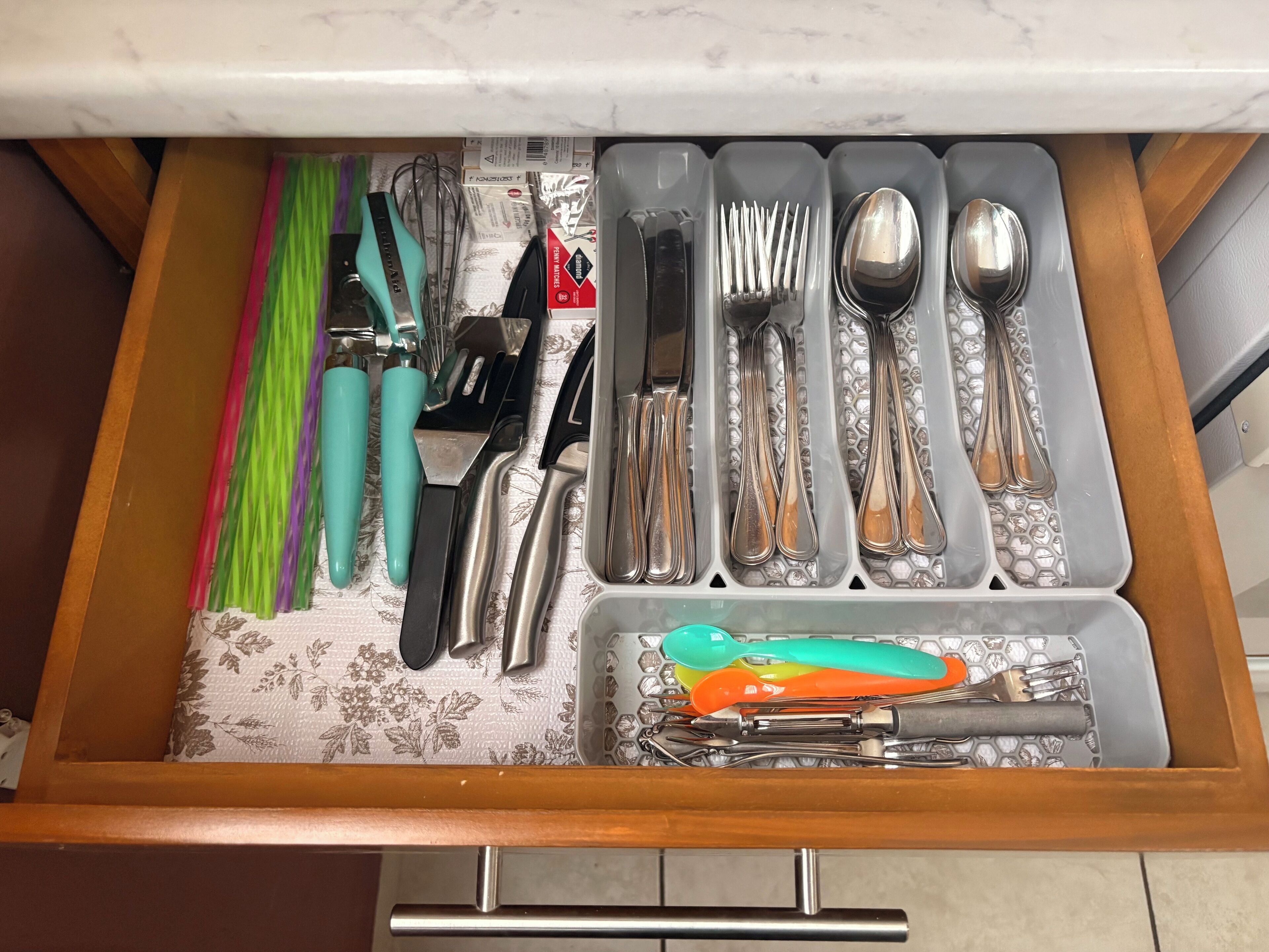 Un cajón con utensilios de cocina ordenados, incluyendo tenedores, cucharas, cuchillos y un rallador.