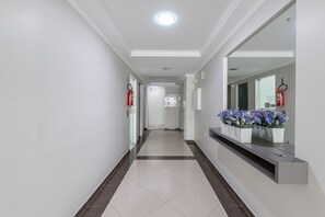 A clean, modern hallway with a tiled floor, a reception desk with a mirror, and a fire extinguisher on the wall. - Apt W/balcony 160m Bombas Beach Col102 (Bombinhas)