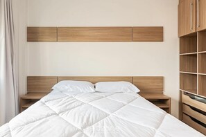 A neatly made bed with a white duvet, a wooden headboard, and a wooden nightstand beside it. - Apt W/balcony 160m Bombas Beach Col102 (Bombinhas)