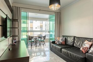 Una sala de estar moderna con un sofá de cuero, un televisor de pantalla plana, una zona de comedor con mesa y sillas, y ventanas amplias con vista a la ciudad.