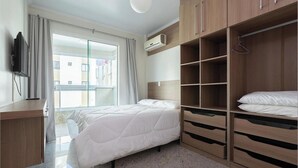 Habitación de hotel con cama, armario, televisor y ventana con cortinas.