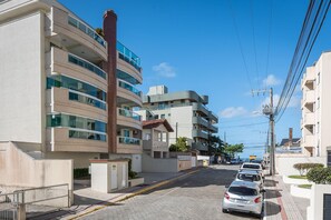 A multi-story residential building with balconies, a paved street, and parked cars. - Apt W/balcony 160m Bombas Beach Col102 (Bombinhas)