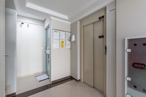 Un pasillo de hotel con una puerta cerrada, una puerta de vidrio que da a una habitación y una pared con avisos.