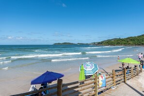 A beach with wooden boardwalk, umbrellas, and people enjoying the water. - Apt W/balcony 160m Bombas Beach Col102 (Bombinhas)