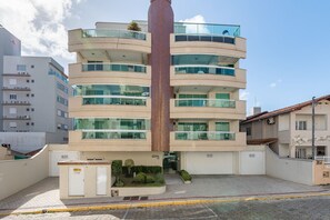 A multi-story building with a central red pillar, balconies, and a gated entrance. - Apt W/balcony 160m Bombas Beach Col102 (Bombinhas)