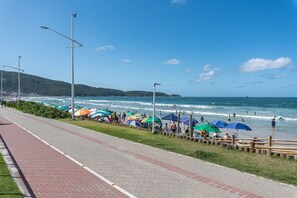 A beachside promenade with a paved walkway, beach umbrellas, and people enjoying the seaside. - Apt W/balcony 160m Bombas Beach Col102 (Bombinhas)