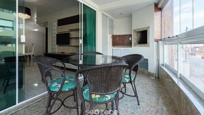 Ein Balkon mit Glastür zu einem Küchenbereich, Korbstühle mit grünen Kissen und Blick auf die Straße.