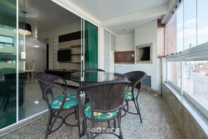 Un balcon doté d’une porte vitrée donnant sur un coin cuisine, des chaises en osier avec des coussins verts, et une vue sur la rue.