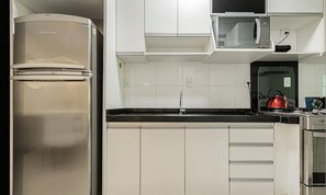 Una cocina con un refrigerador de acero inoxidable, un microondas y una tetera en la encimera.