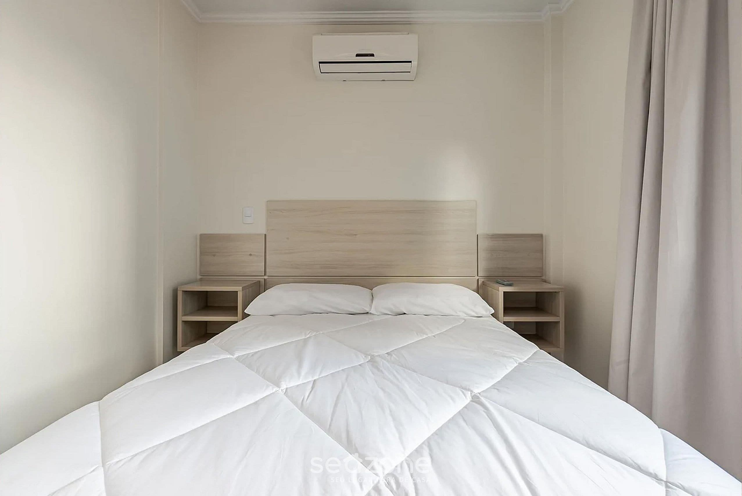A neatly made bed with a quilted white duvet, a wooden headboard, and two bedside tables with lamps.