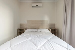 A neatly made bed with a quilted white duvet, a wooden headboard, and two bedside tables with lamps. - Apt W/balcony 160m Bombas Beach Col102 (Bombinhas)
