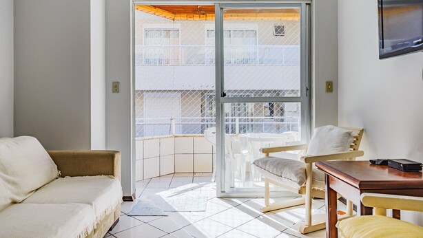 A room with a sofa, a wooden table, and a chair. There is a sliding glass door leading to an outdoor balcony.