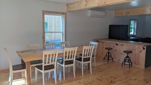 A dining area with a wooden table and chairs, a kitchen counter with stools, and a window with a view of the outdoors. - The Cabins at Timber Ridge - #3 - Brand new cabins nestled in the woods of NH (Tamworth)