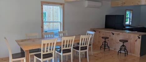 A dining area with a wooden table and chairs, a kitchen counter with stools, and a window with a view of the outdoors.