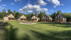 A row of wooden cabins with a circular seating area in the center. - The Cabins at Timber Ridge - #3 - Brand new cabins nestled in the woods of NH (Tamworth)