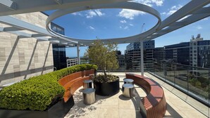 Terraza en la azotea con un espacio de estar curvo, un árbol en maceta y vistas de los edificios circundantes.