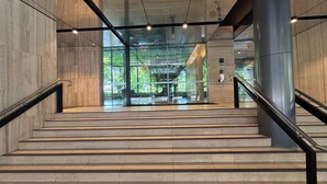 Una escalera moderna con barandillas de vidrio y vistas a un parque a través de puertas de cristal en la parte superior.