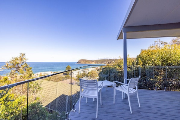 A balcony with a view of the ocean, white chairs, and a glass railing.