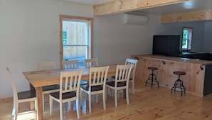 Un comedor con mesa y sillas de madera, una encimera de cocina con taburetes y un ventanal con vistas al exterior.